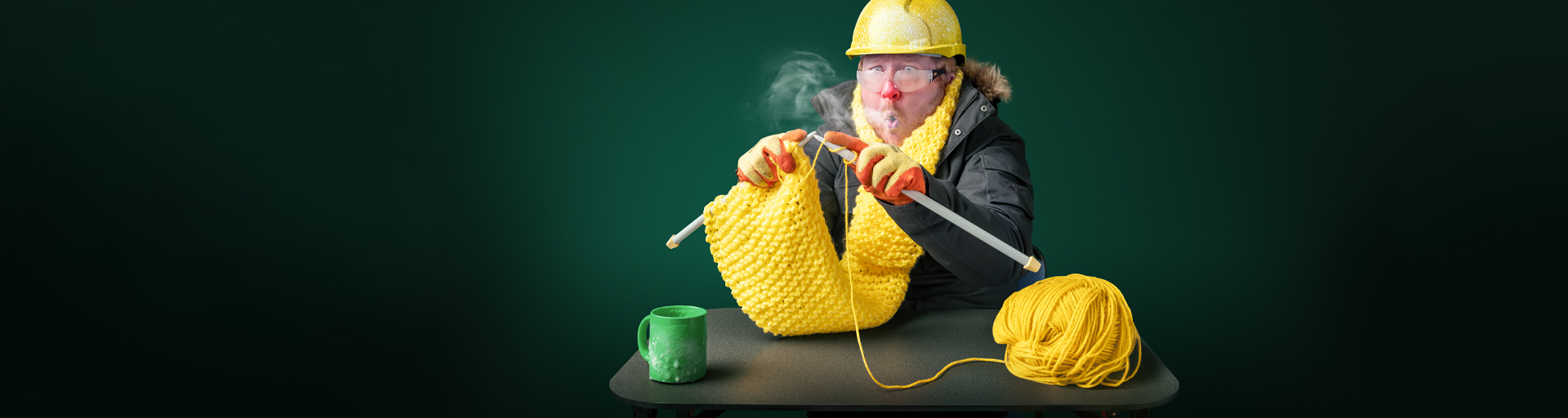 Man sitting at a desk feeling cold knitting a yellow scalf 